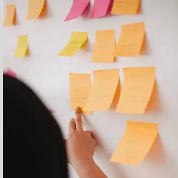 Professionnel en informatique organisant des tâches de développement et de gestion de projet sur un mur de brainstorming avec des post-it colorés.